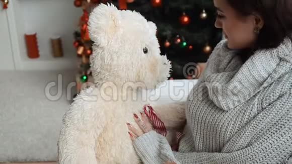 可爱的女孩坐在圣诞树旁手里拿着一只大玩具熊视频的预览图
