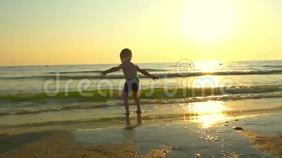 小男孩在海滩上的海水中跳跃以缓慢的速度在日落的背景下视频的预览图