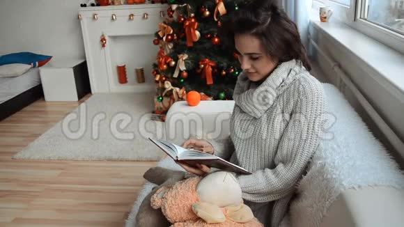漂亮的女孩坐在沙发上的圣诞树旁拿着记事本望着窗外视频的预览图