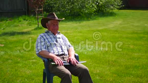 老人累了坐在一张椅子上戴着帽子在一片绿色的草坪上视频的预览图