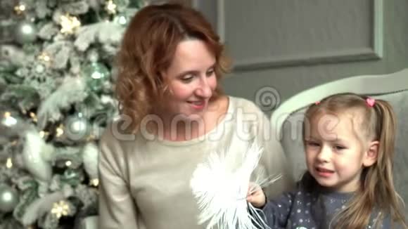 母亲带着女儿坐在圣诞树上坐在沙发上笑母亲在白发苍苍的女儿身上挠痒痒视频的预览图