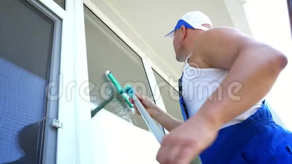 白人英俊男子清洁服务工人穿着蓝色工作服戴着一顶帽子擦擦擦窗户视频的预览图