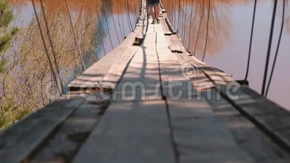 一家人妈妈爸爸和女儿的特写腿走在河上的旧吊桥上视频的预览图