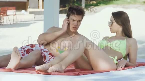 帅哥打电话和他的女孩在海滩上休息视频的预览图