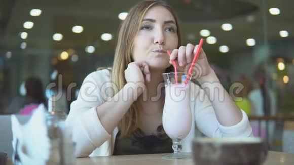 年轻漂亮的女孩在咖啡馆喝牛奶鸡尾酒视频的预览图