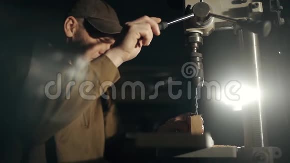 一个穿着特殊制服的专业木匠正在车间的木块上钻一个洞视频的预览图