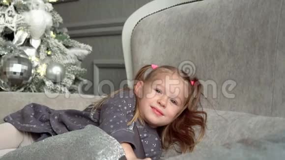 那个微笑着的金发小女孩在一棵杉树的沙发上玩耍小女孩看着电话慢蛾视频的预览图