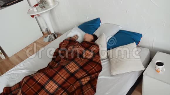 年轻的黑发女人躺在毯子下面的床上视频的预览图