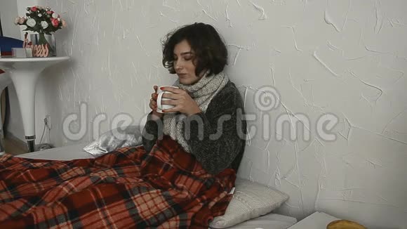 生病的女人躺在床上穿着毛衣喝着热饮料视频的预览图