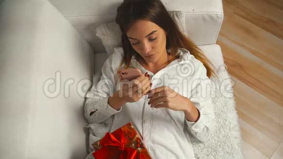 女孩躺在沙发上拿着礼物在手机上写着一条信息视频的预览图