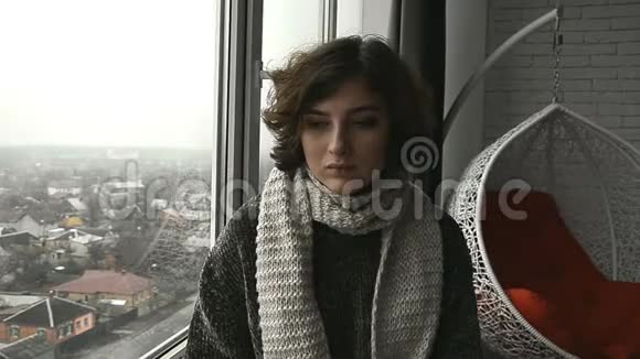 一个穿着毛衣和围巾的女人坐在窗边喉咙痛视频的预览图