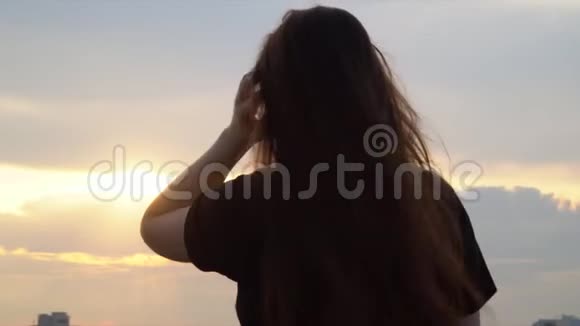 美丽的长发女孩挽起一只手屋顶上女孩的黑暗轮廓风玩女孩视频的预览图