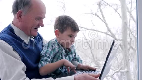 电脑游戏爷爷带着孙子手拿手提电脑在家窗户上视频的预览图
