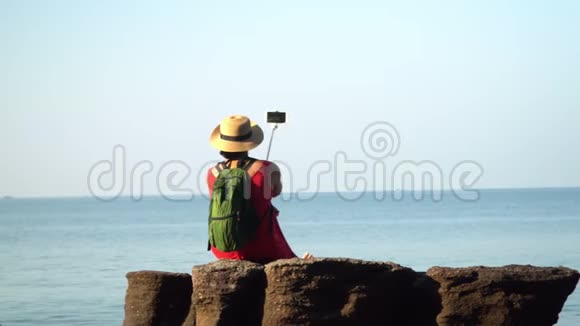 来自背包和帽子的女人通过自拍棒自拍在岛上阳光明媚的一天一个女人视频的预览图