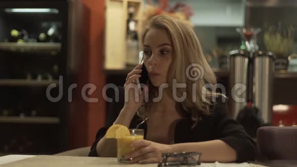 年轻女子在桌旁用手机说话咖啡屋里有橙汁视频的预览图
