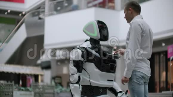 一个男人和机器人机器人站在一起问他问题并通过点击机器人身体上的屏幕来寻求帮助视频的预览图