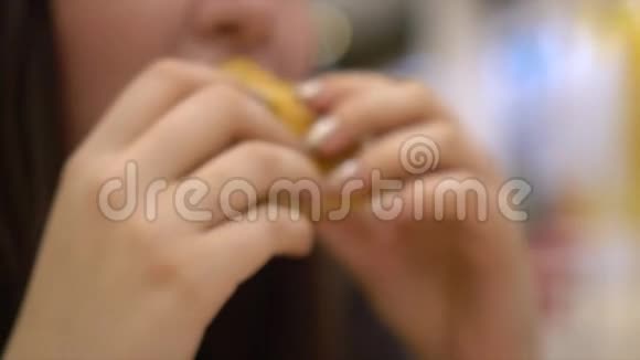 那个女孩吃汉堡包那个留着长发的女孩坐在购物中心的一张小桌子旁快餐把手举起来视频的预览图