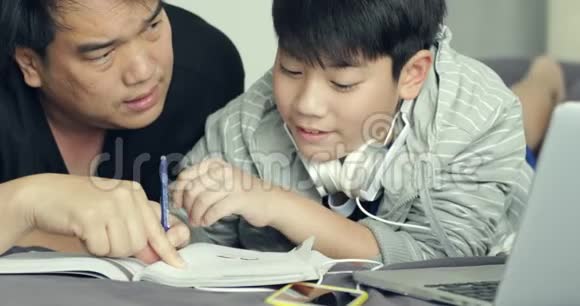 当男孩在家做家庭作业时亚洲父亲帮助他的小儿子视频的预览图