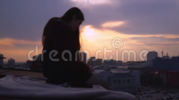 这个女孩坐在hdaniye的屋顶上手里拿着智能手机那个留着深色长发的女孩坐着顶着屋顶视频的预览图