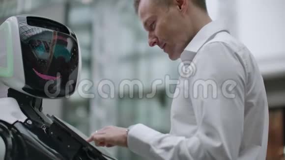 一个男人和机器人机器人站在一起问他问题并通过点击机器人身体上的屏幕来寻求帮助视频的预览图