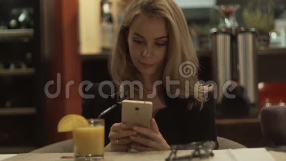 戴眼镜的年轻女子坐在咖啡馆的桌子上用手机打电话视频的预览图