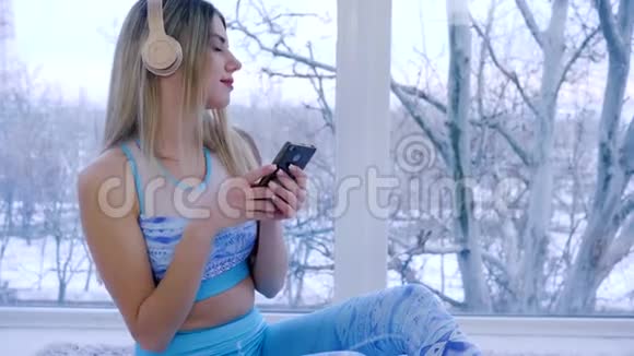 手里拿着手机的女人在窗户的背景下通过耳机听旋律视频的预览图