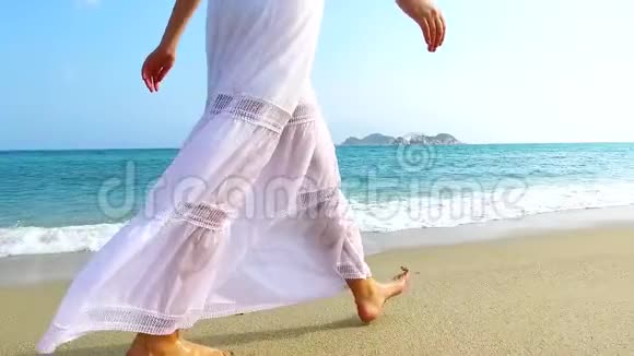 阳光明媚的一天穿着白色连衣裙的女孩在沙滩上散步慢动作视频的预览图