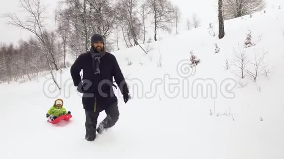 冬锋跟随父亲拉着红色雪橇在雪域与孩子爸爸儿子或女儿雪上雪橇家庭视频的预览图