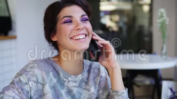 漂亮的年轻女人坐在咖啡馆里打电话她在笑漂亮的年轻女性休闲装视频的预览图