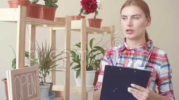 小生意一个穿着格子衬衫和条纹围裙的女孩站在纸上用一张纸把数据输入其中视频的预览图