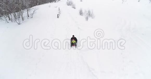 冬天的空中跟随父亲骑着红色的雪橇和孩子在下雪的下坡爸爸儿子或女儿斯诺的雪橇视频的预览图
