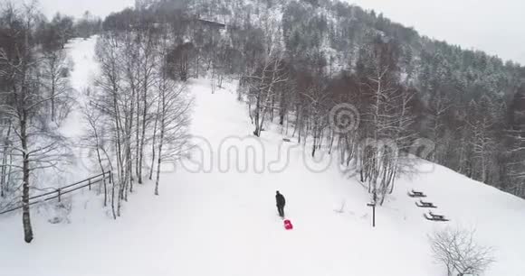 空中跟随男子父亲拉着红色雪橇在冬天的雪上升爸爸带着雪橇上雪家庭成员享有视频的预览图