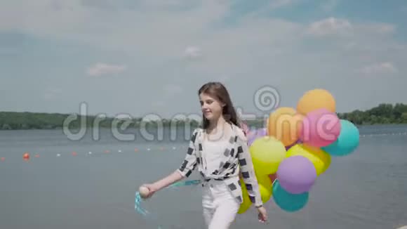 美丽的女孩带着五颜六色的气球走在河湾上看着水视频的预览图