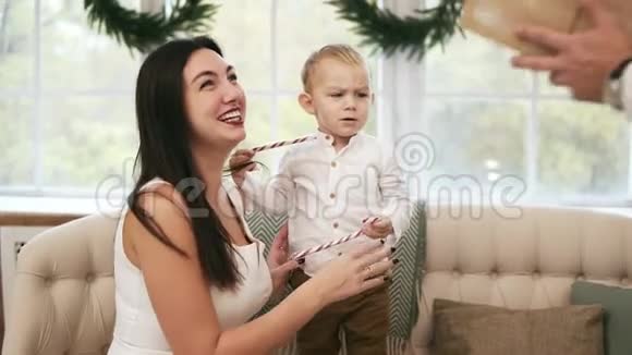 年轻的母亲穿着白色连衣裙接受丈夫的圣诞礼物亲吻他金发可爱的蹒跚学步的孩子视频的预览图