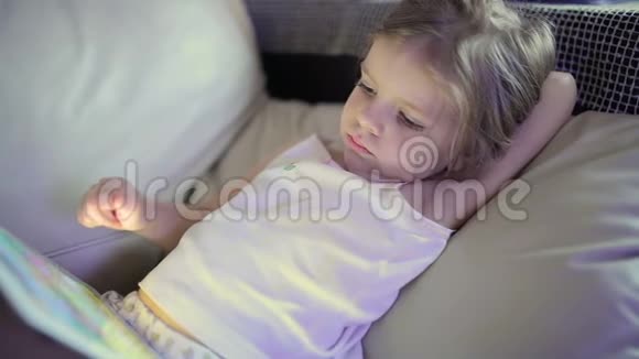 小可爱的女孩躺在沙发上玩平板电脑视频的预览图