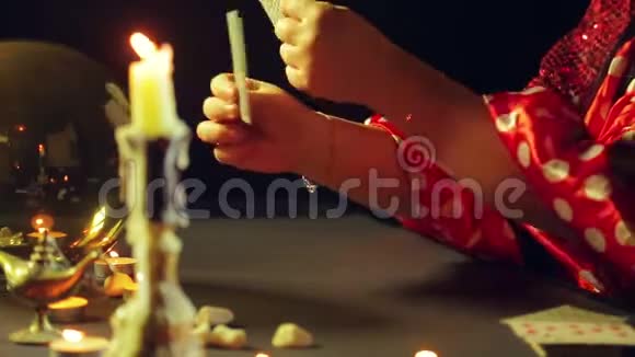 一个年轻的吉普赛人穿着红色的衣服在烛光下的桌子上用算命的卡片来读未来平均计划视频的预览图