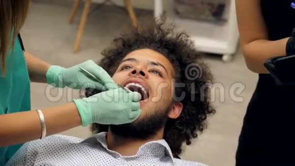 一位牙医检查一位年轻人的牙齿牙医助理正在写应该修理的东西视频的预览图