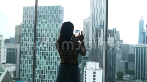 站在窗口的女游客使用智能手机在吉隆坡摩天大楼的手机上拍照视频的预览图