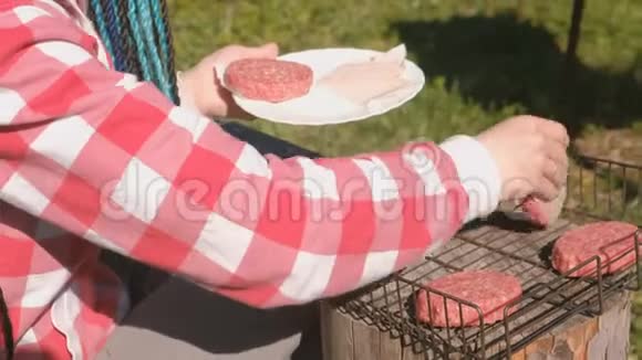 年轻的女人把切子放在烤架上特写双手她穿着格子粉色衬衫有蓝色的辫子视频的预览图