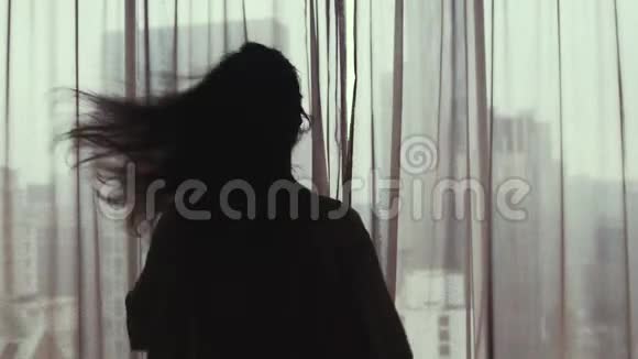 迷人的年轻女子拉开窗帘看着公寓里的窗户从高处欣赏城市景色3840x2160视频的预览图
