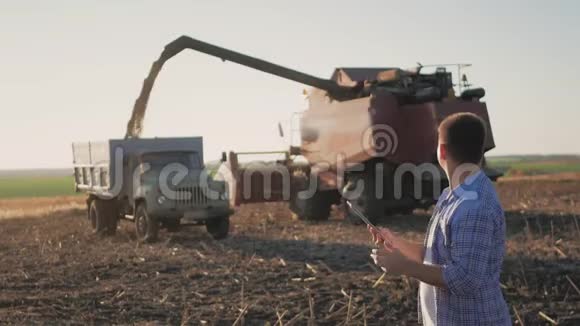 英俊的农民与平板站在联合收割机的背景农民使用现代技术触摸平板电脑视频的预览图