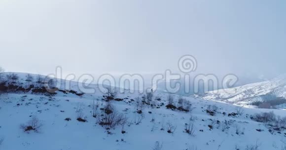 侧面空中飞越冬季雪山山顶与妇女徒步雪鞋晴天雾蒙蒙的云雾在上升阿尔卑斯山视频的预览图