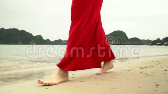 女人双腿合拢背景上的海洋那个穿红色衣服的女人在海滩上散步漂亮女孩的特写视频的预览图