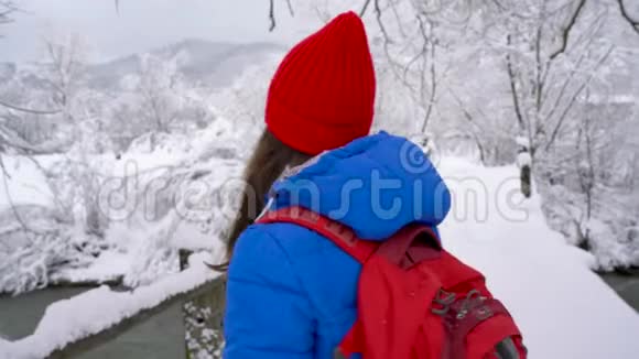 年轻女子穿过大桥过河用智能手机拍了一张美丽的冬天雪的照片视频的预览图