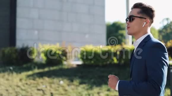 年轻的商人带着太阳镜在户外听智能手机上的音乐跳舞他走在办公室附近视频的预览图