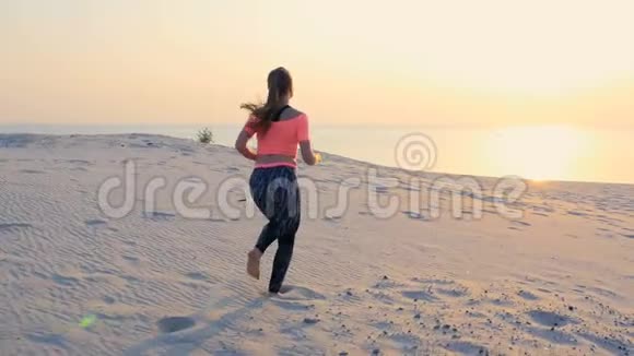 健康年轻的运动美女沿着沙滩奔跑在海滩上在夏天走向太阳在日出视频的预览图