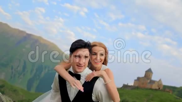 新娘和新郎在他们婚礼的那天在雄伟的群山中在一个夏天的旧教堂里玩得很开心视频的预览图