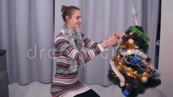 年轻快乐的女人穿着圣诞毛衣微笑着用玩具装饰圣诞树慢镜头视频的预览图