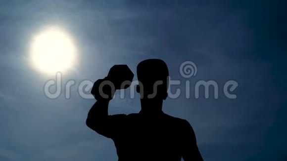 强壮的健美运动员戴着帽子一只手举着哑铃顶着太阳夏天的蓝天晴朗视频的预览图