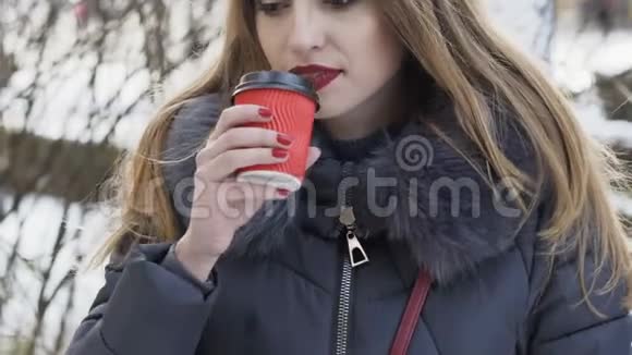 漂亮的女孩在冬天寒冷的街道上喝热咖啡慢慢地视频的预览图